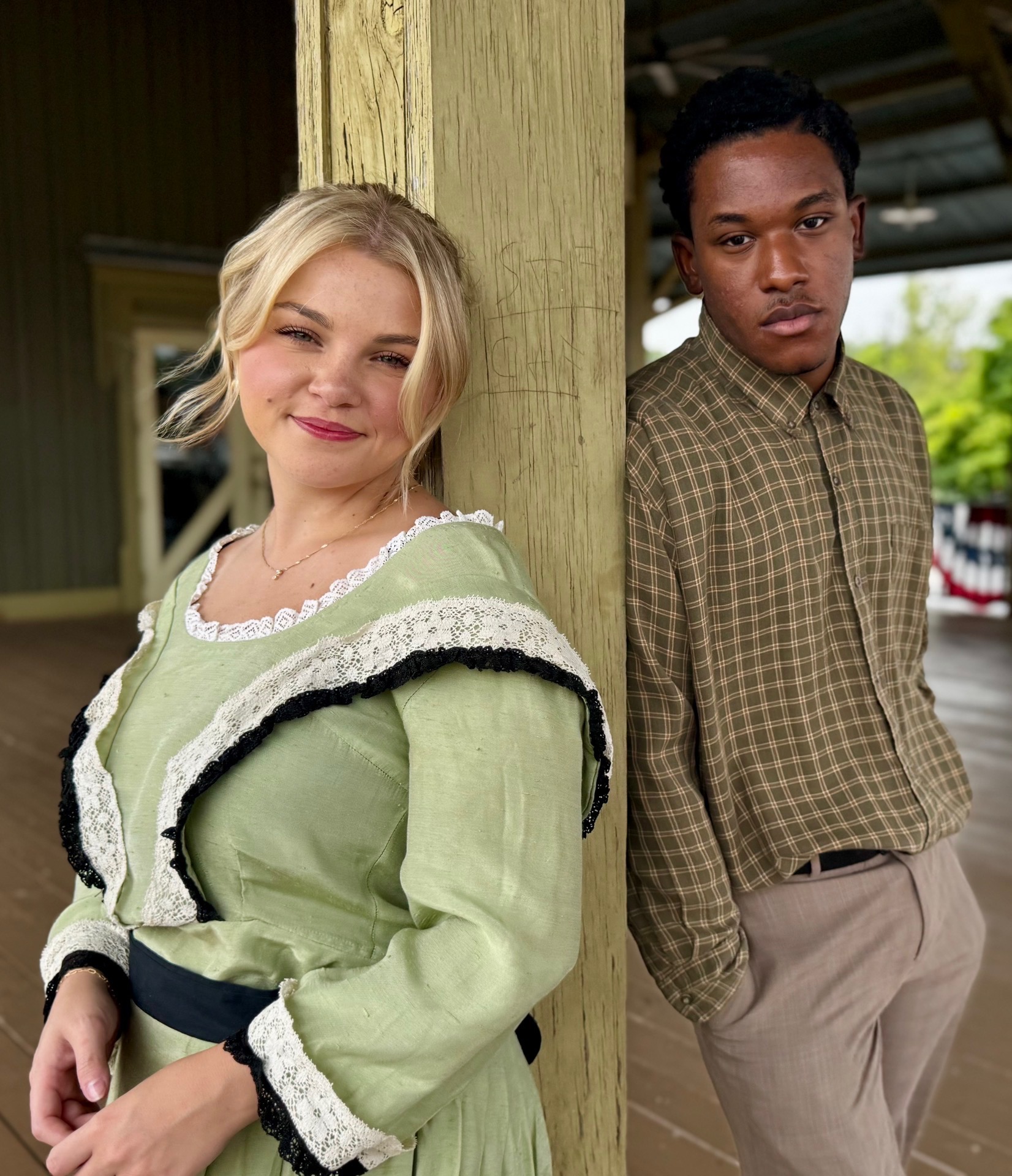Two lead cast members leaning against a depot column in costume