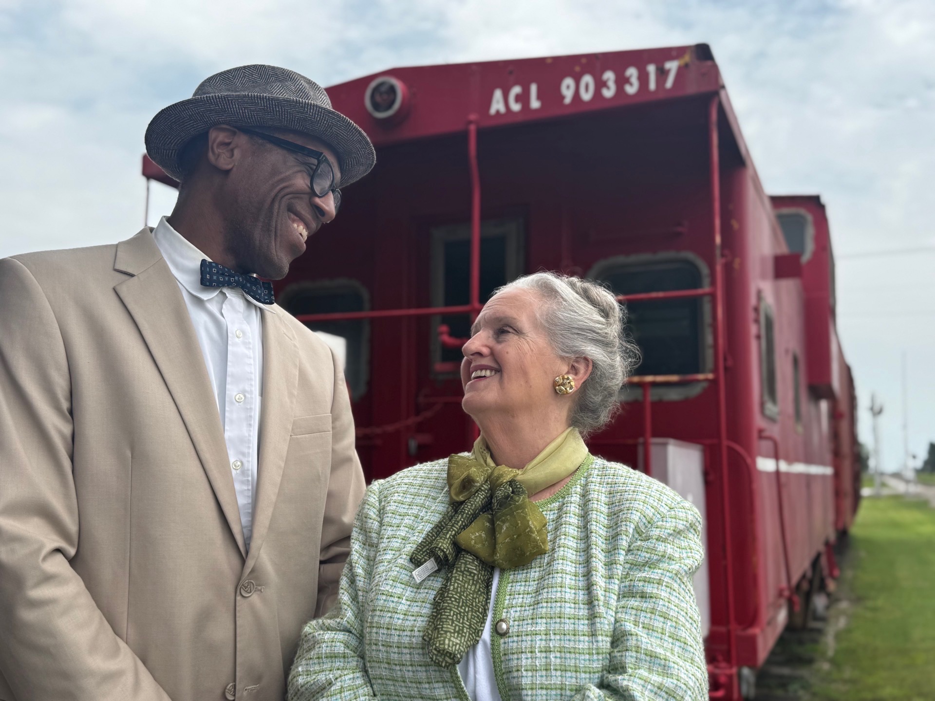 Two cast members of The Depot standing before a historic red railcar